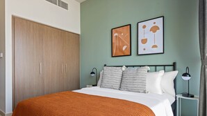 A bedroom with a bed, two bedside tables, a wardrobe, and two wall art pieces.