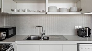 A kitchen with a double sink, a toaster, a coffee maker, and shelves with glassware and dishes.