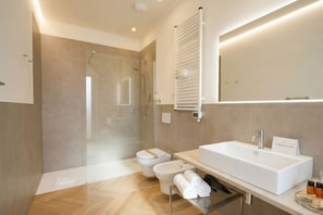 Un baño moderno con cabina de ducha de vidrio, un lavamanos blanco y un perchero.