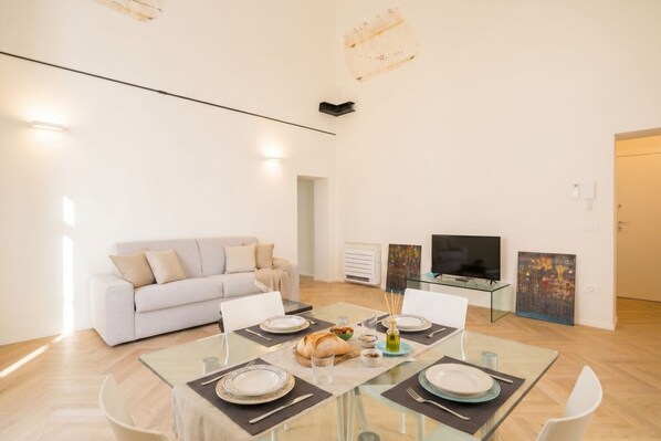 Una sala de estar moderna con un sofá, una mesa de comedor para cuatro personas, un televisor de pantalla plana y obras de arte en las paredes.