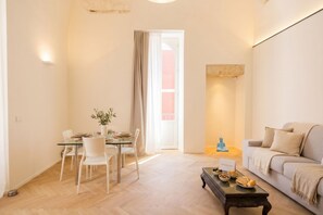 A modern living room with a glass dining table, white chairs, a sofa, and a coffee table. - PalazzoTorre 101 - Luxury Apartment & Terrace (Bari)