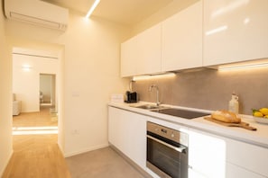 Una cocina moderna con armarios blancos, un lavamanos de acero inoxidable y un horno empotrado.