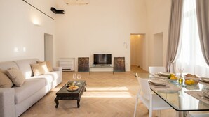 Ein modernes Wohnzimmer mit Sofa, Couchtisch, Fernseher und Essbereich mit Glastisch und Stühlen.