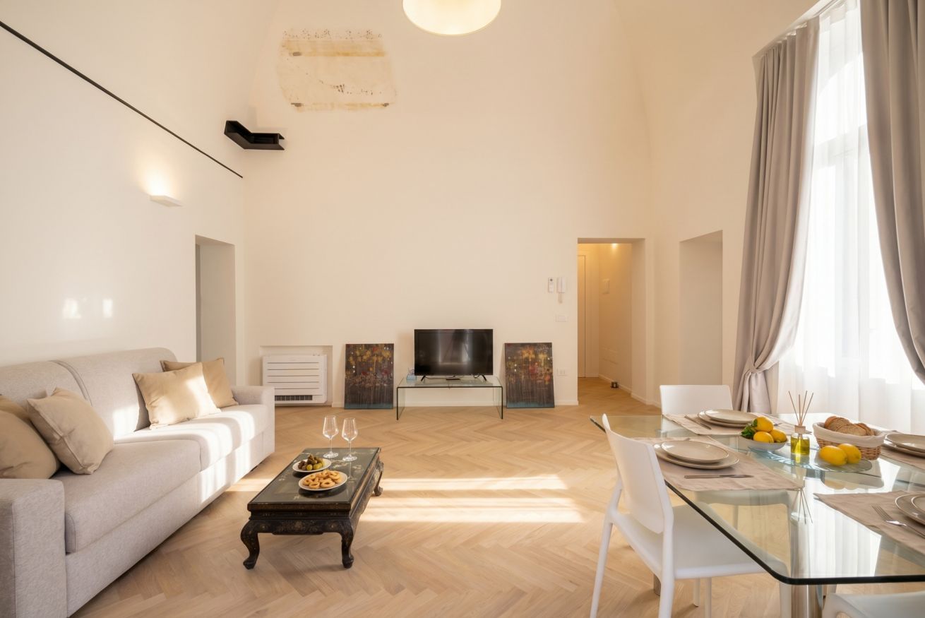 Ein modernes Wohnzimmer mit Sofa, Couchtisch, Fernseher und Essbereich mit Glastisch und Stühlen.