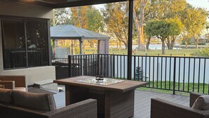 A covered outdoor patio with wicker furniture, a table, and a view of a lake and trees. - Waterlink Retreat - canal views with easy access to both the canal and the river (South Yunderup)