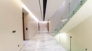 Een moderne hotelgang met marmeren vloer, glazen balustrades en een trap.