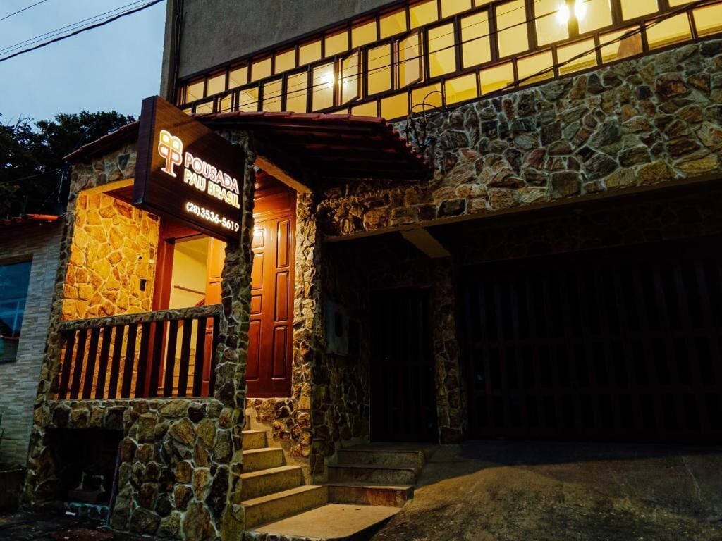 A stone building with a sign reading "Pousada Pau Brasil" and a wooden door.