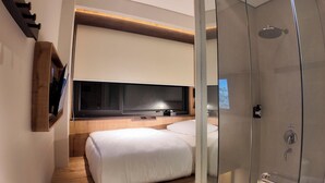 A modern hotel room with a bed, a TV mounted on the wall, and a glass shower enclosure.