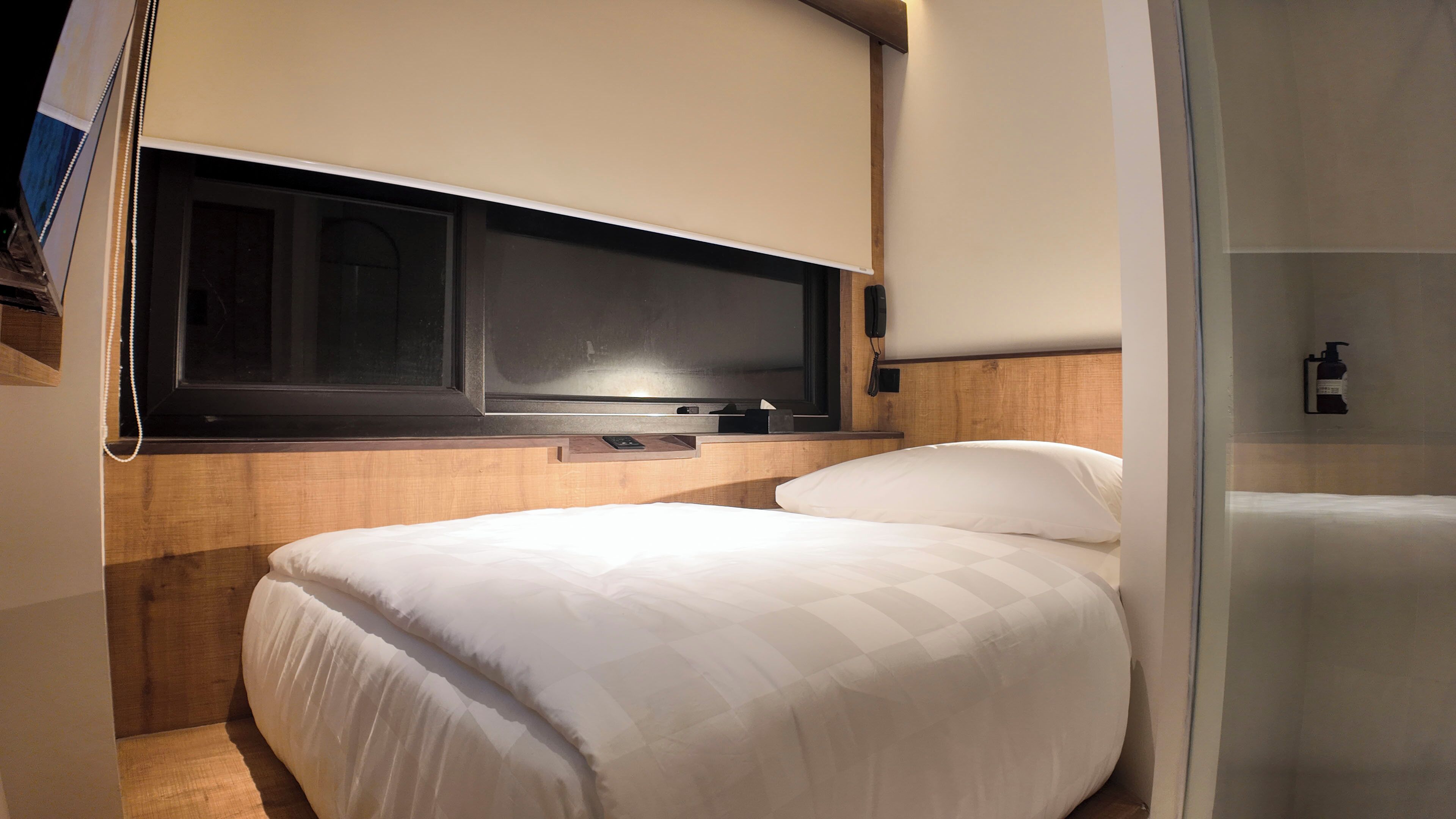 A compact bedroom with a bed, a mounted television, and a small bedside table.