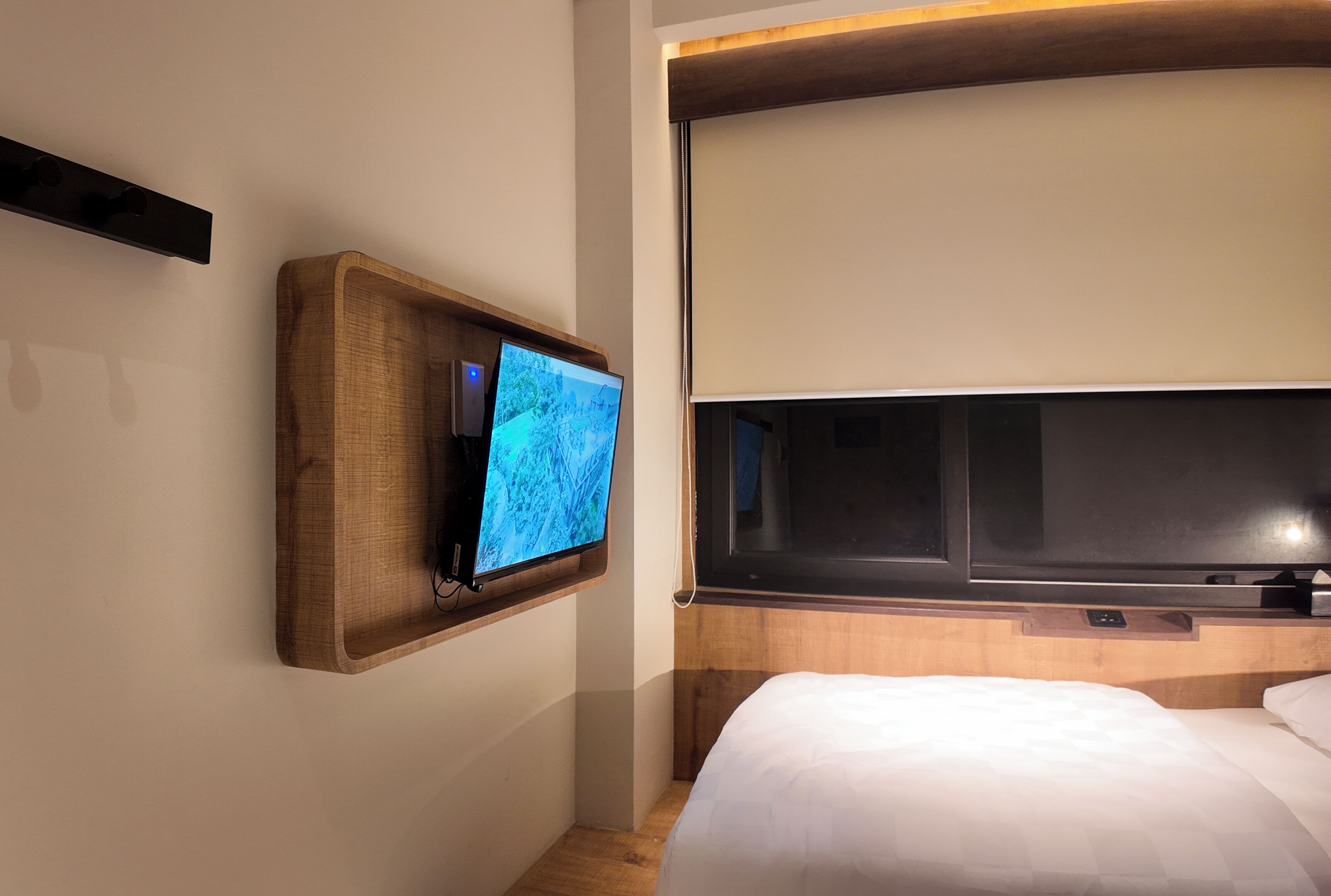 A hotel room with a wooden TV stand, a large flat-screen TV, a bed with white bedding, and a wooden headboard.