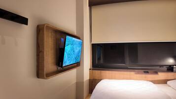 A hotel room with a wooden TV stand, a large flat-screen TV, a bed with white bedding, and a wooden headboard.