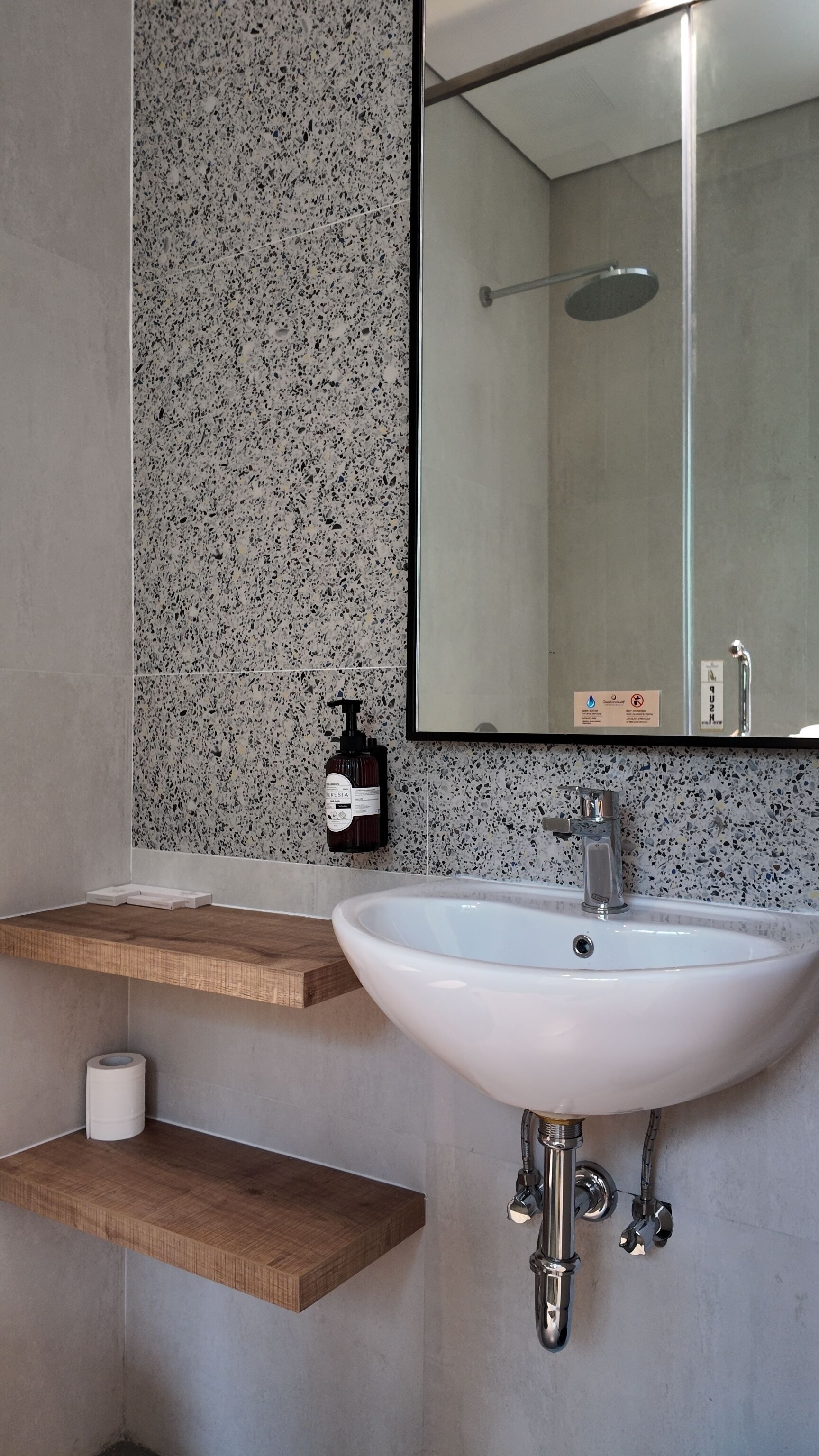 Un baño con lavamanos blanco, espejo, ducha y dispensador de jabón.