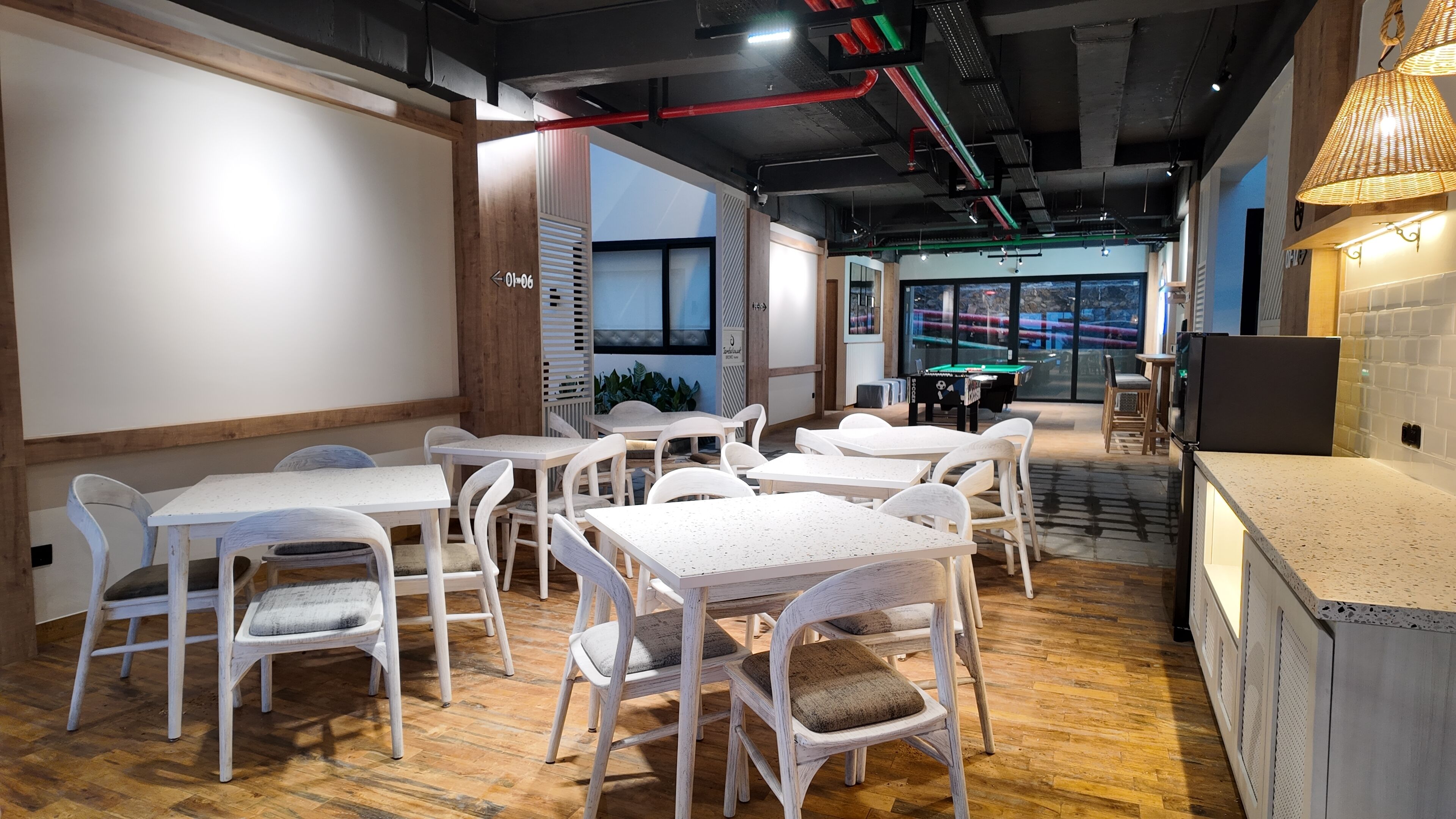 Un comedor moderno con mesas y sillas blancas, una mesa de billar y una cocina con refrigerador.