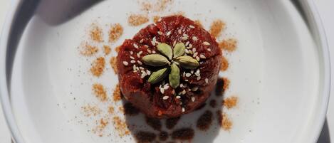 A white plate with a central food item, possibly a dessert or appetizer, garnished with seeds and spices.