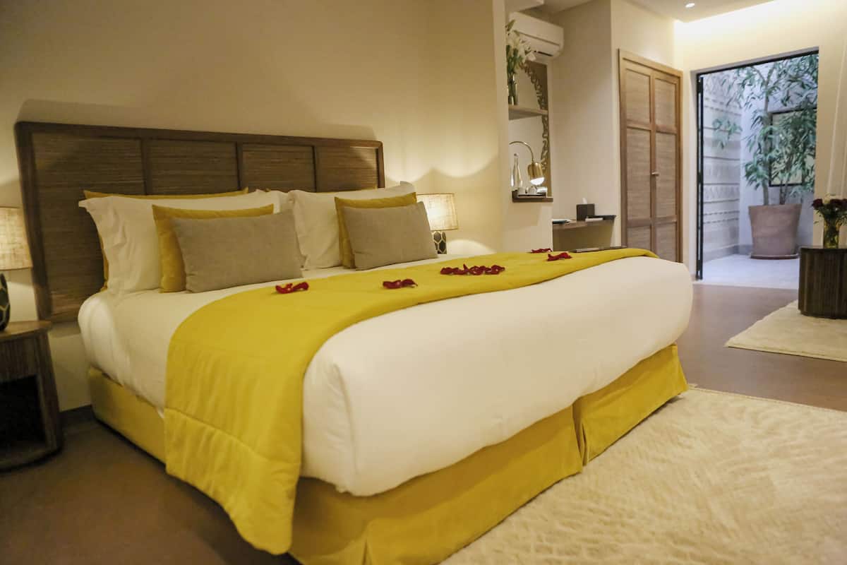 A neatly made bed with a yellow bedspread and white pillows, a bedside lamp, and a wooden headboard.