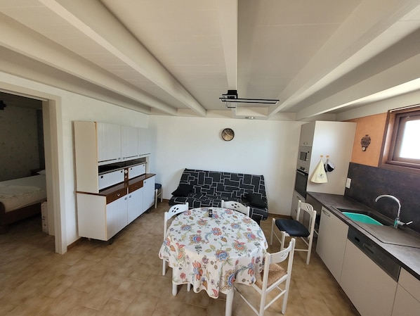 A compact kitchen with a dining area, a sofa, and a small table with floral tablecloths.