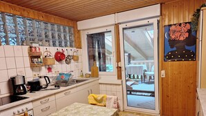 A kitchen with white cabinets, a dining table with a floral tablecloth, a coffee maker, and a window with a view of the outdoors.
