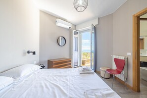 Een slaapkamer met een bed, een dressoir, een rode stoel, een radiator en een balkon met uitzicht.