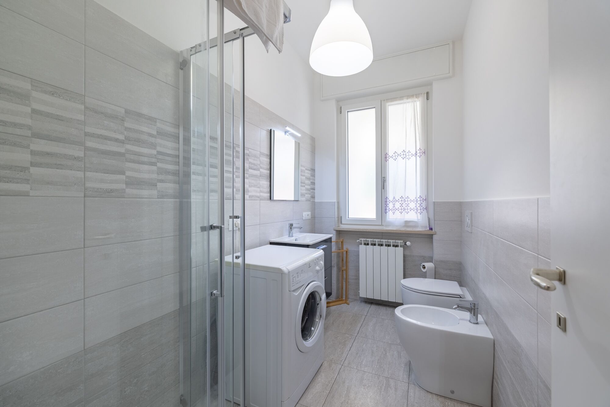 Een moderne badkamer met een douchecabine van glas, een ingebouwde wasmachine, een toilet en een wastafel.
