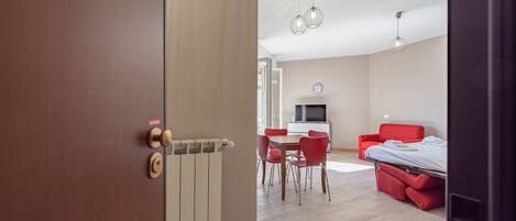 A modern living room with a dining area, a red sofa, a TV, and a ceiling light fixture.