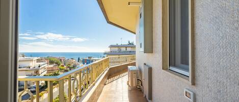 A balcony with a view of the sea and neighboring buildings.