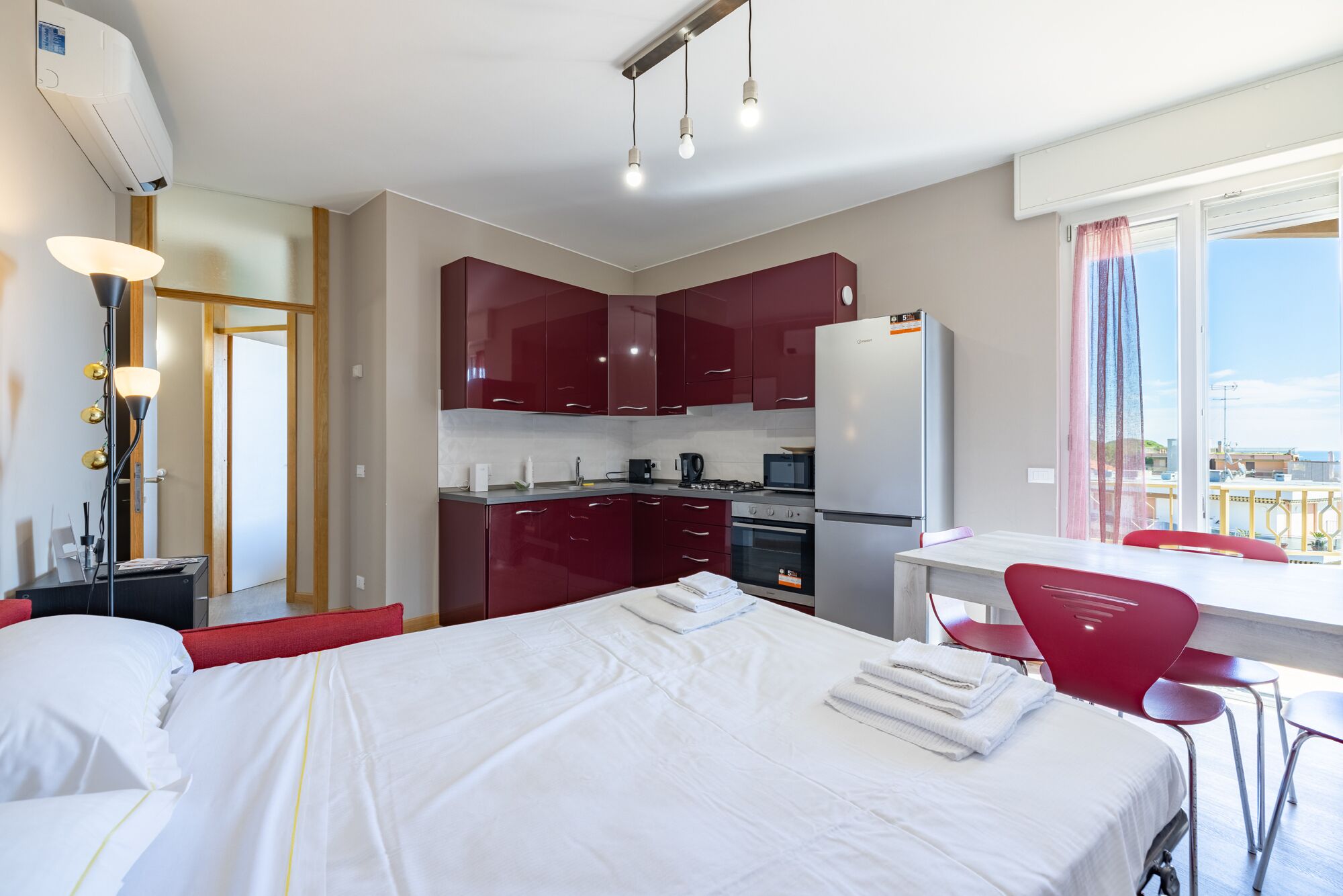A hotel room with a bed, a desk with a chair, a kitchenette, and a window with a view.
