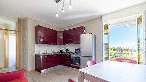 A modern kitchen with dark red cabinets, a stainless steel refrigerator, and a dining area with a white table and red chairs. - Sun & Sea Homes by Wonderful Italy (Sanremo)