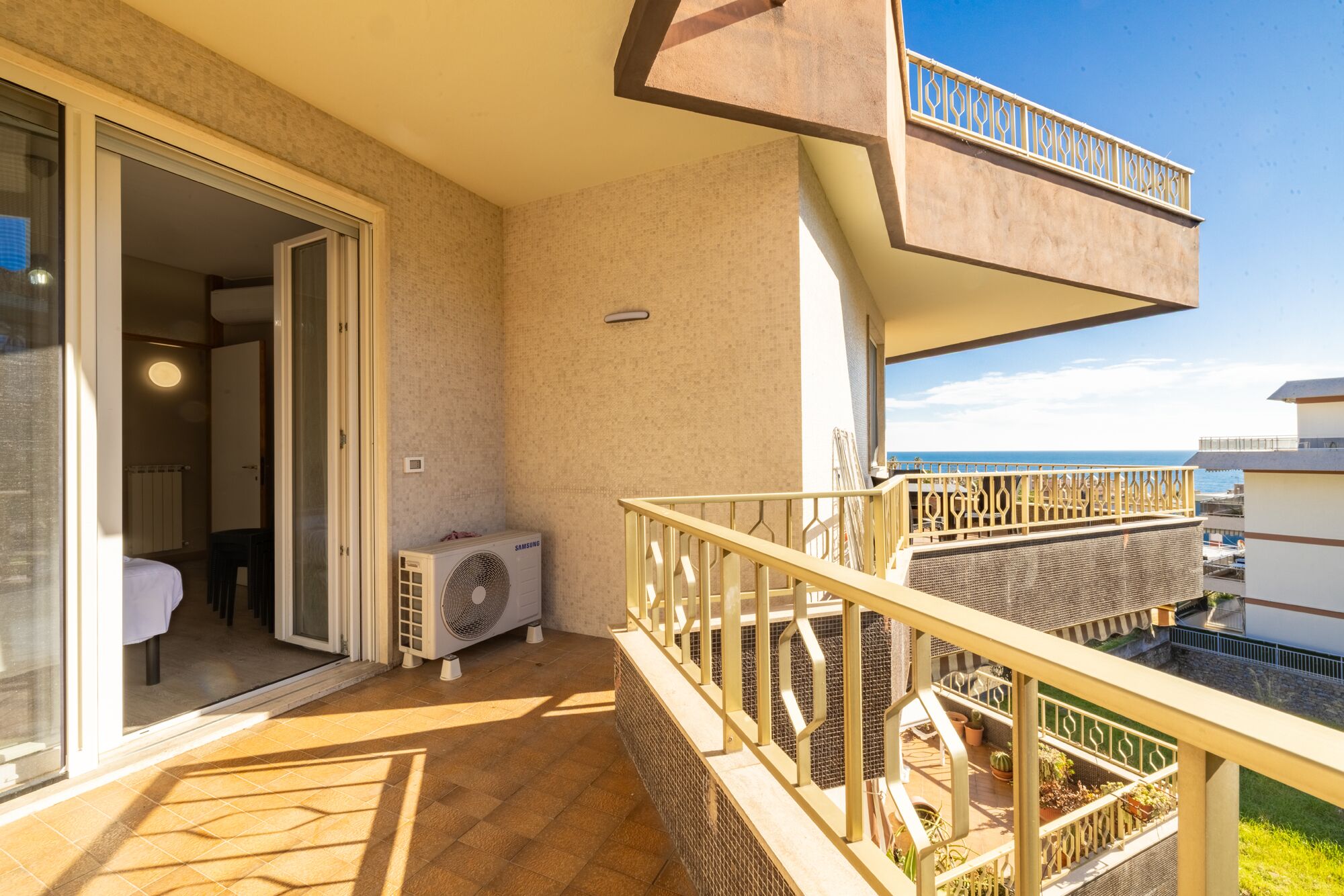 Un balcon avec vue sur la mer, un climatiseur Samsung et une porte donnant sur une pièce.