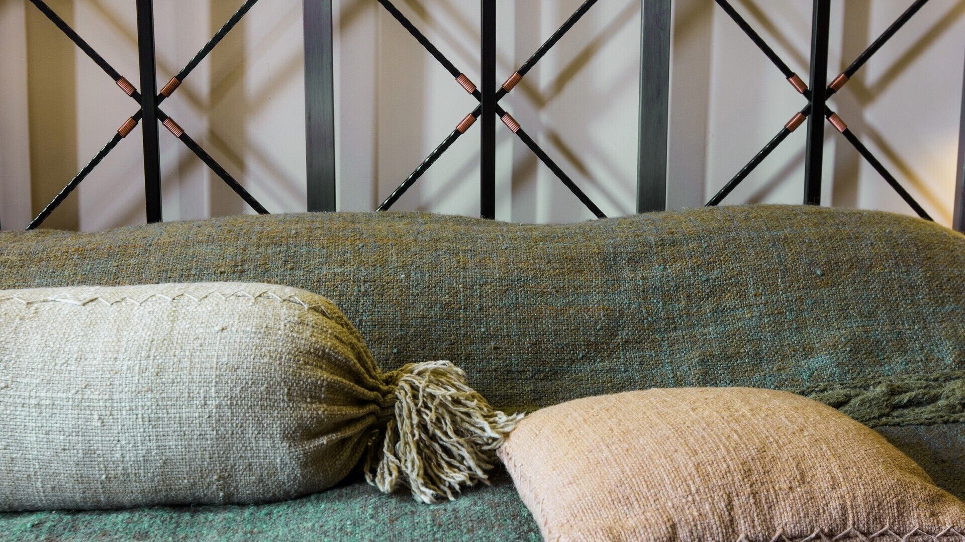 A sofa with a textured fabric and a decorative tassel pillow against a wall with a geometric pattern.