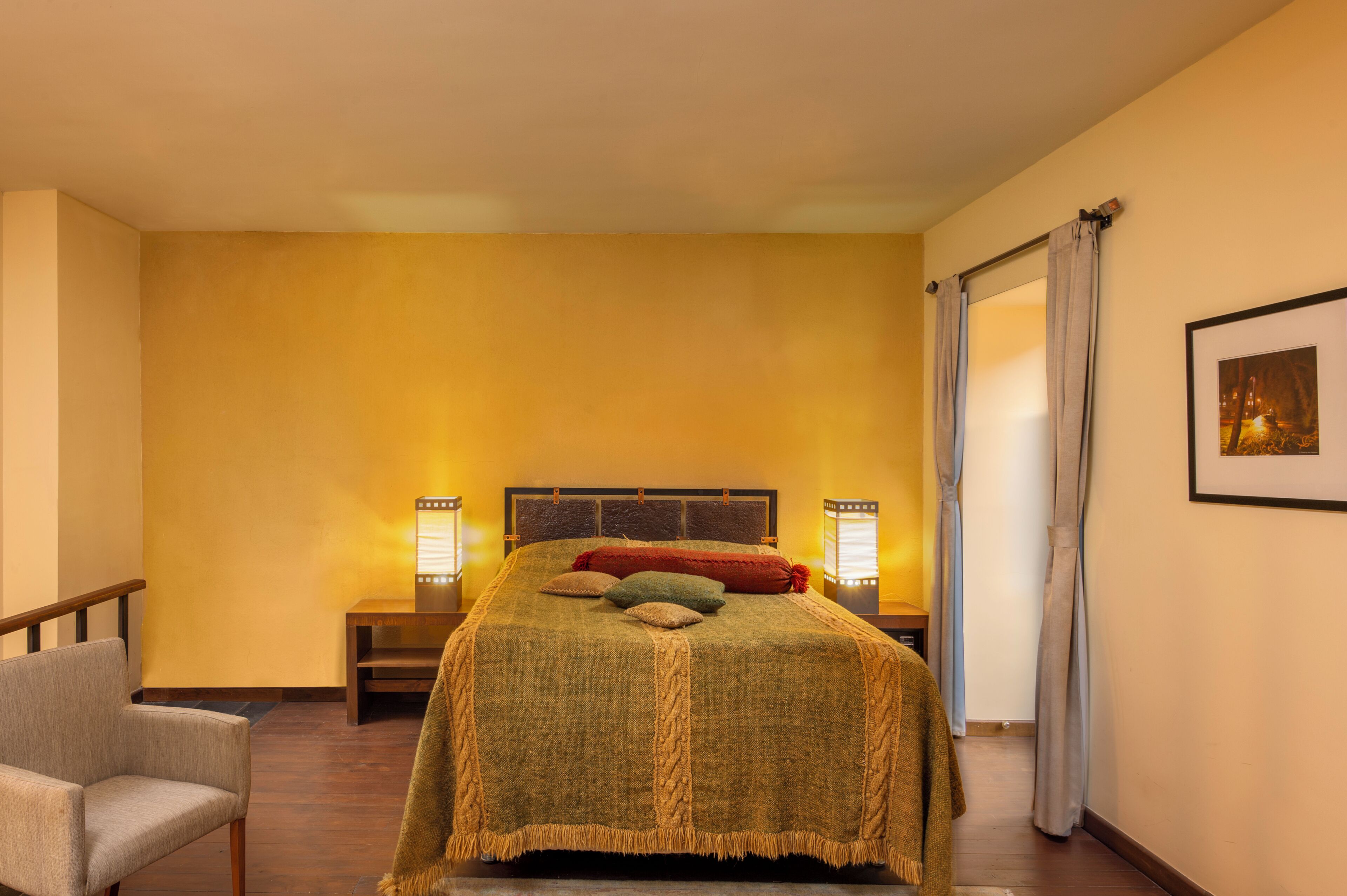 A hotel room with a bed, a chair, and a nightstand with a lamp.