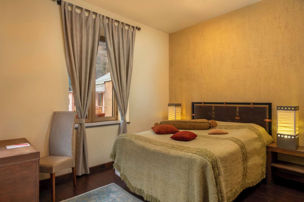 Ein Schlafzimmer mit Bett, Stuhl, Schreibtisch und einem fenster mit Vorhängen.