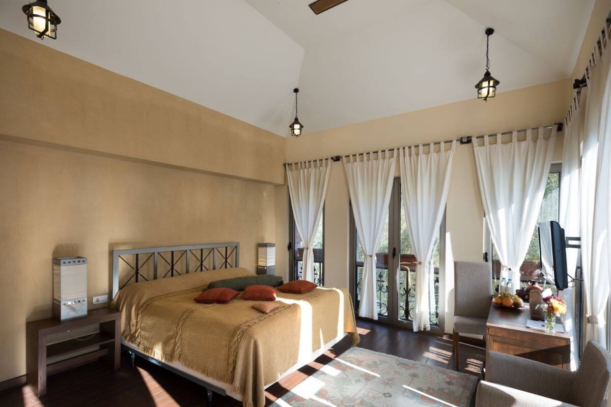 Ein geräumiges Schlafzimmer mit einem großen Bett, einem Schreibtisch mit Stuhl und Blick ins Freie durch große Fenster.