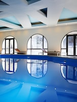 Una piscina interior con reflejos claros, ventanas arqueadas grandes y un diseño moderno de techo.