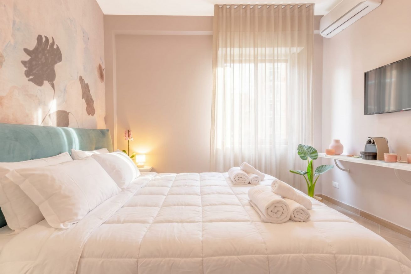 Une chambre d’hôtel avec un lit, une télévision, une plante et une fenêtre avec des rideaux.