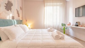 Een hotelkamer met een bed, een televisie, een plant en een raam met gordijnen.