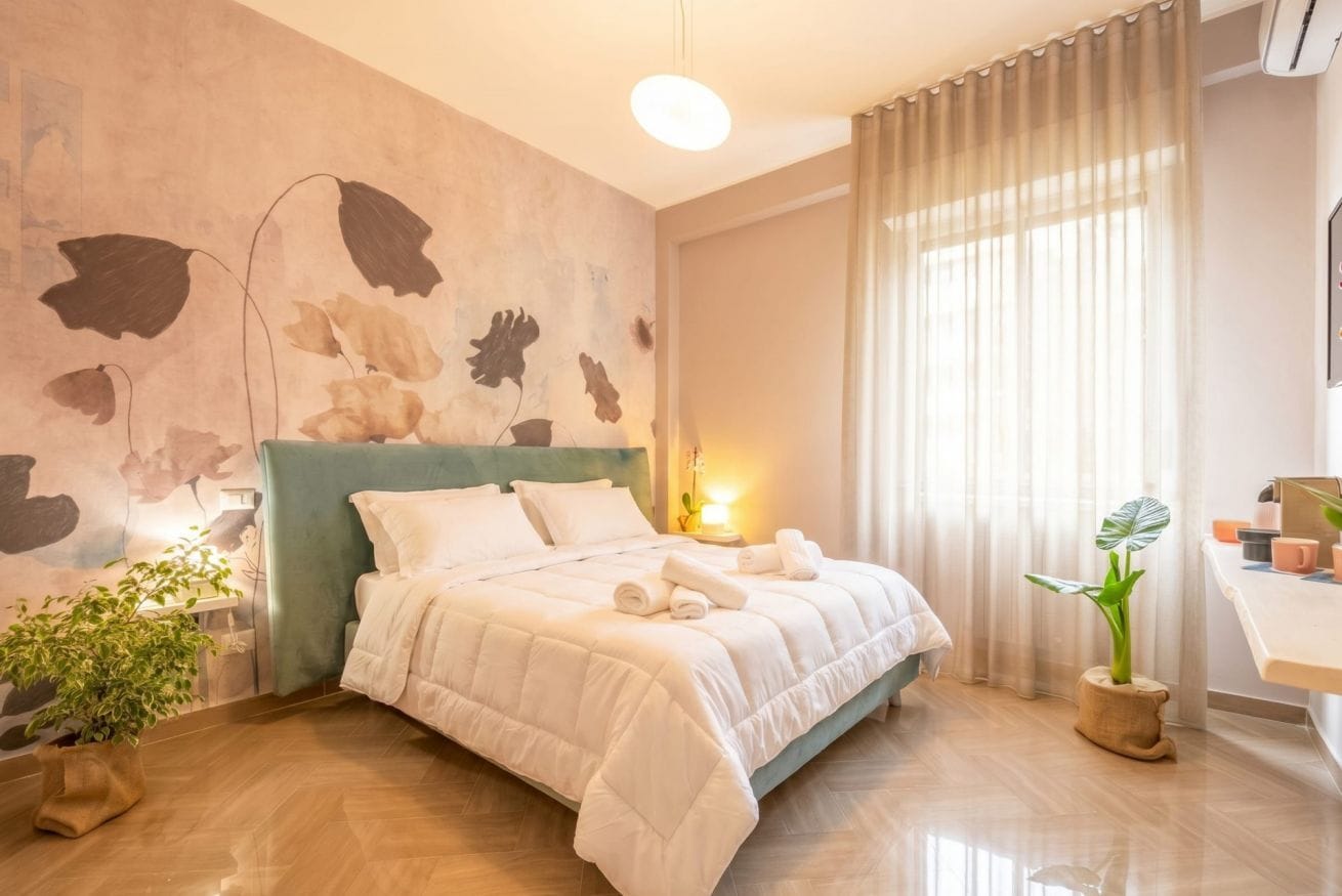 Une chambre à coucher moderne avec un grand lit, une table de chevet, une plante en pot et un mur orné d’un motif de feuilles.