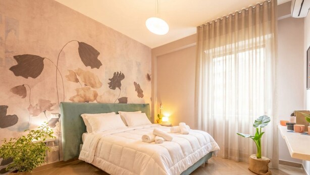 Een moderne slaapkamer met een groot bed, een nachtkastje, een kamerplant en een muur met een bladmotief.