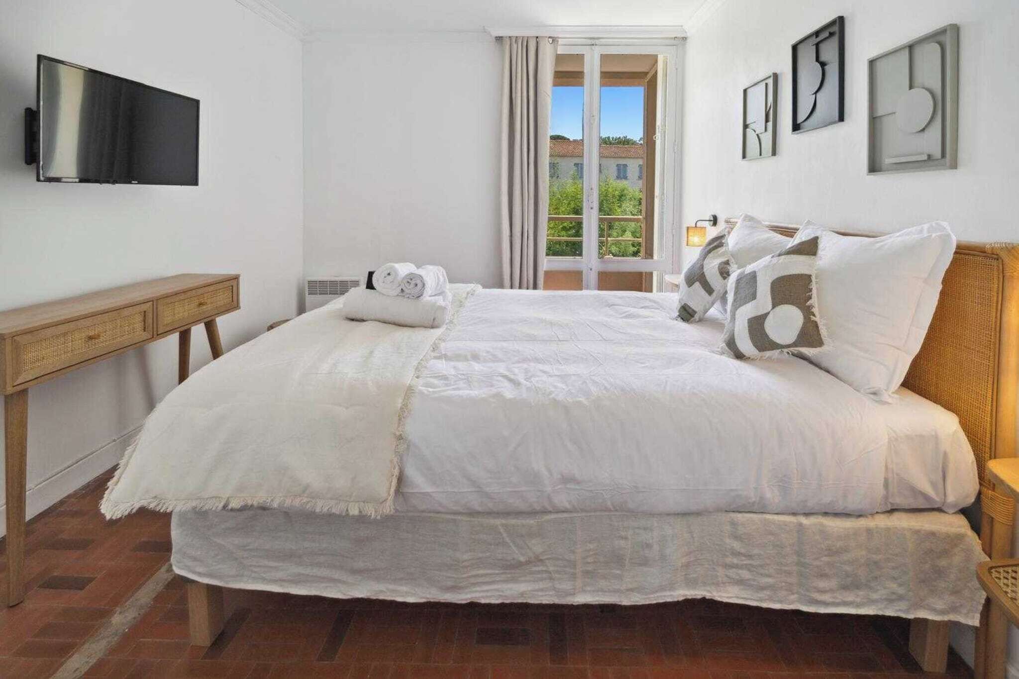 A bedroom with a bed, a TV, a window with curtains, and artwork on the wall.