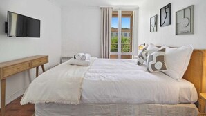 A bedroom with a bed, a TV, a window with curtains, and artwork on the wall. - Apt 2BR/4P-Balcony Saint-Tropez (Saint-Tropez)
