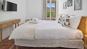 A bedroom with a bed, a TV, a window with curtains, and artwork on the wall.