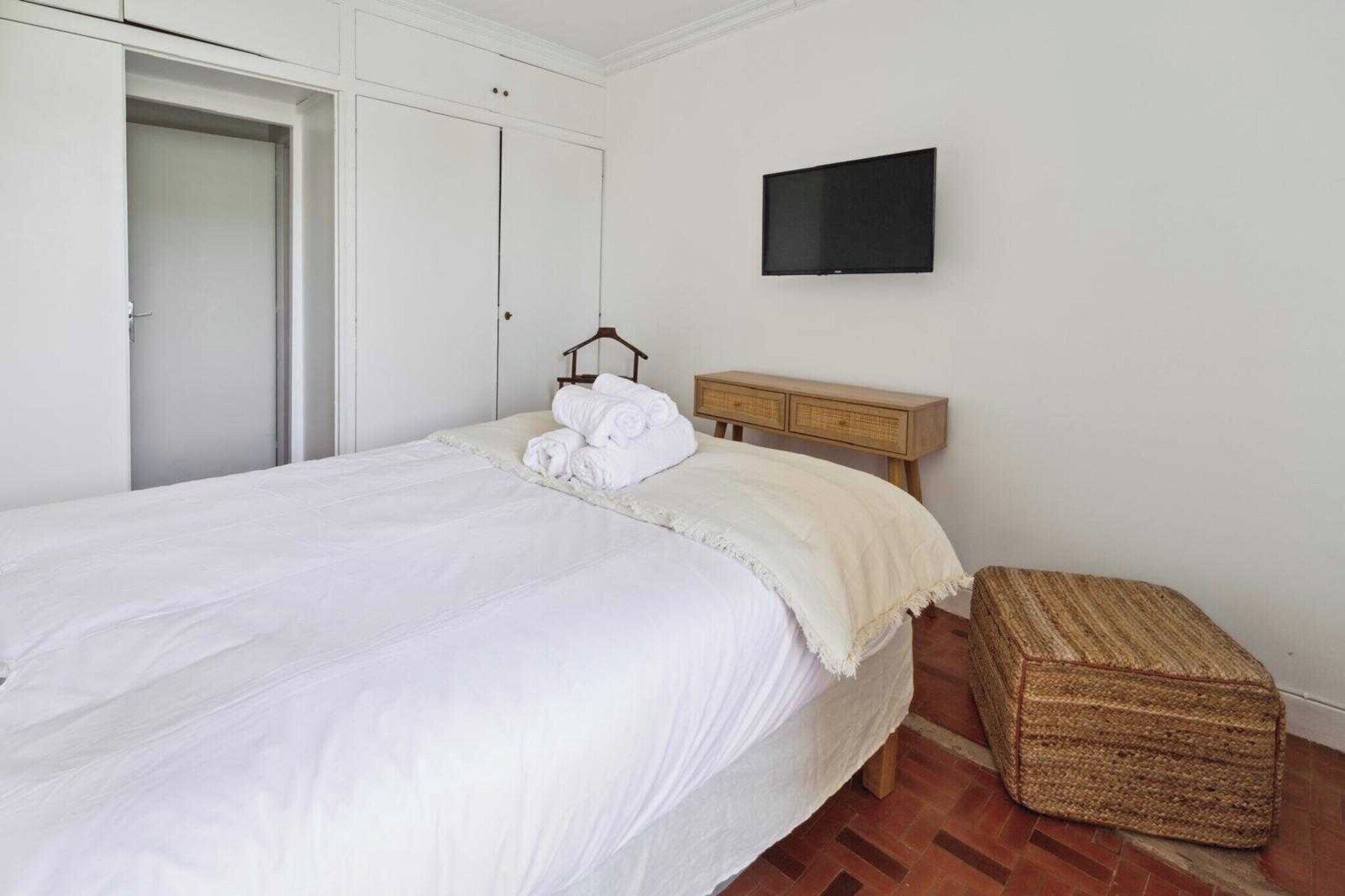 A bedroom with a bed, a television, a wardrobe, and a small wooden chest of drawers.
