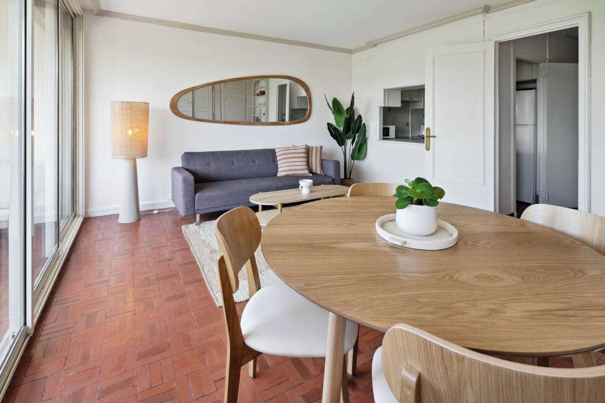 A dining area with a wooden table, chairs, a sofa, a lamp, and a potted plant.