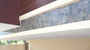 A covered outdoor area with a checkered floor, stone wall, and a metal vent. - Zenova Stays (Chennai)