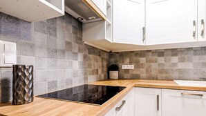 Eine moderne Küche mit weißen Schränken, einer schwarzen Induktionskochplatte und einer gefliesten Spritzschutzwand.