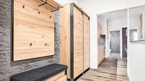 Un interior moderno con un mueble de pared de madera, un banco y una cocina visible a través de una puerta abierta.