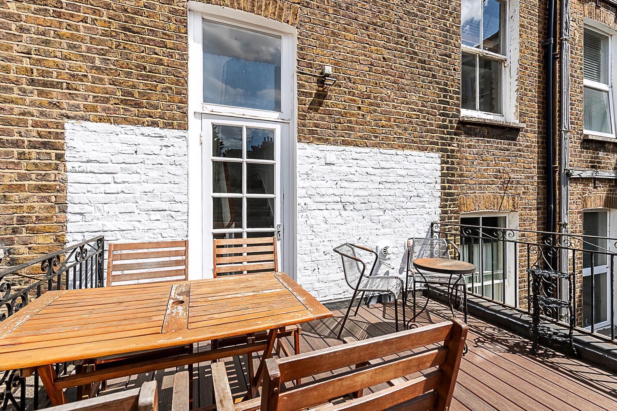A wooden deck with a table and chairs, a white brick wall, and a window.