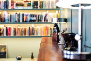 A bookshelf filled with books, a small figurine, and a lamp on a wooden table. - Stylish West Kensington Flat With Character (London)