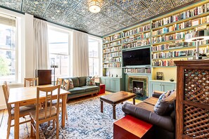 Ein gemütliches Wohnzimmer mit Kamin, Bücherregal, Fernseher und einer gemusterten Decke.