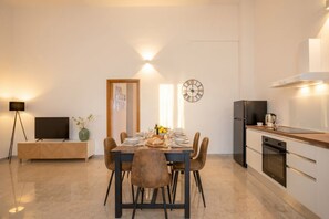 Een moderne keuken met een eettafel voor vier personen, een klok aan de muur en een televisie op een kast.