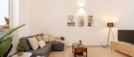A modern living room with a grey sofa, a small round table, a floor lamp, and abstract wall art.